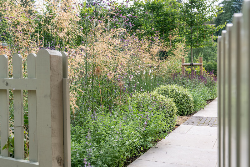 Open gate leading along garden path with flower border